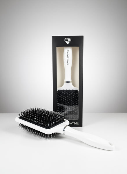 White hairbrush with 'Wayne' branding next to a black packaging box on a reflective surface.