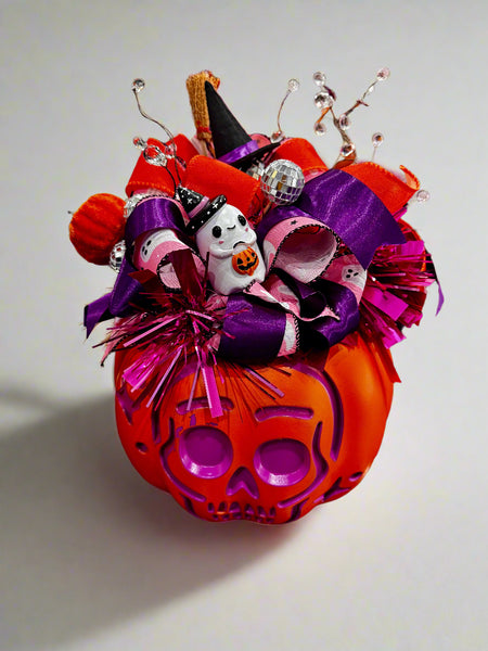 Decorative Halloween pumpkin with colorful ribbons and a ghost figure on a reflective surface.