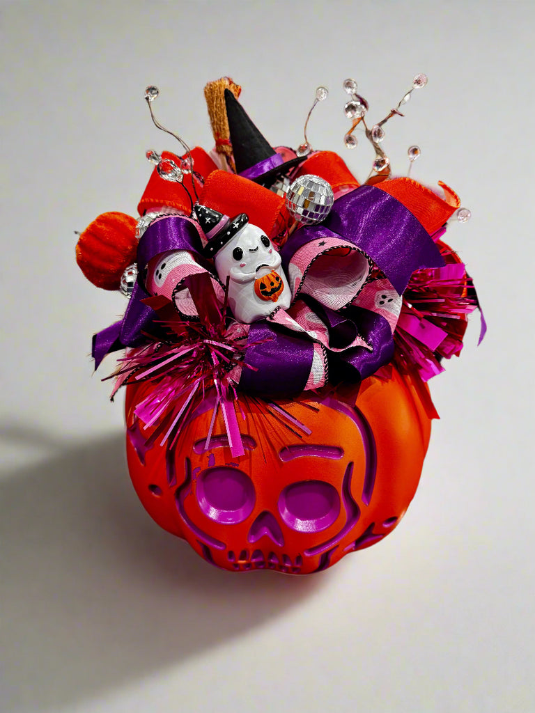 Decorative Halloween pumpkin with colorful ribbons and a ghost figure on a reflective surface.